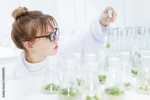 In a biological laboratory, a girl assistant examines test tubes with grown plants. Eco-friendly plants for farms