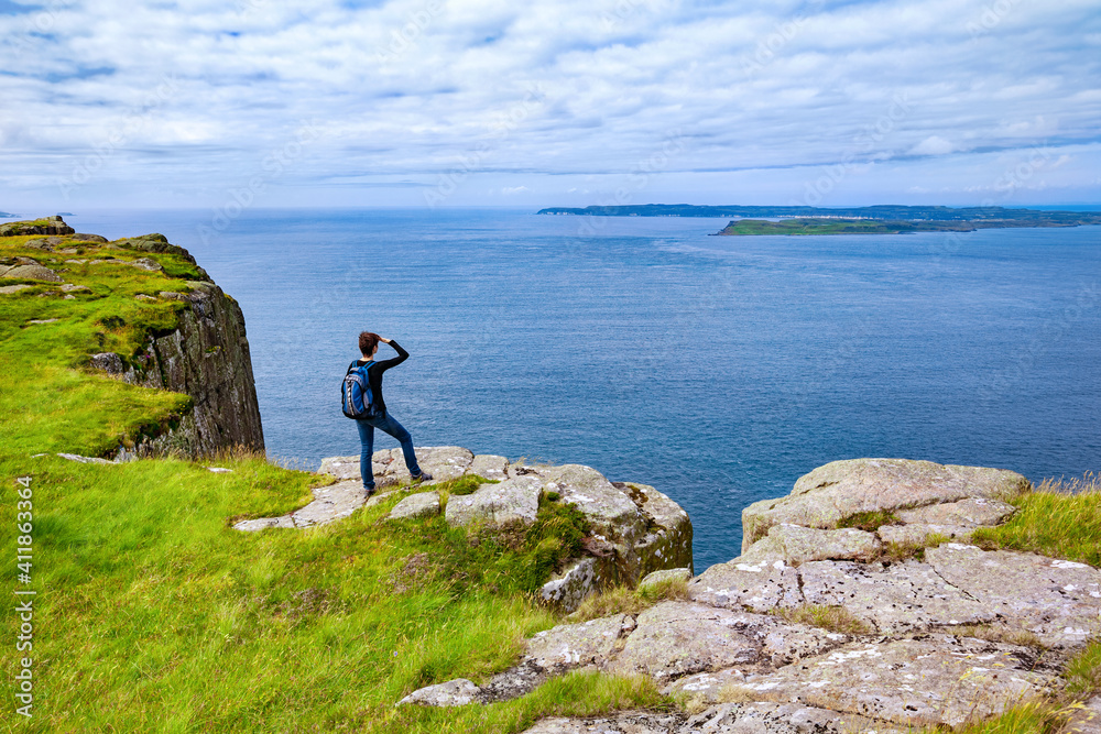 tourist with backpack standing on the cliff Fair Head, Northern Ireland, UK