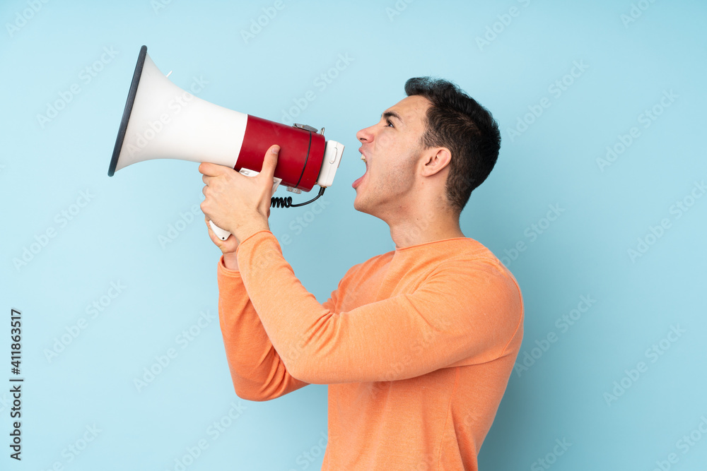 Young caucasian handsome man isolated on blue background shouting through a megaphone Young caucasian handsome man isolated on blue background shouting through a megaphone