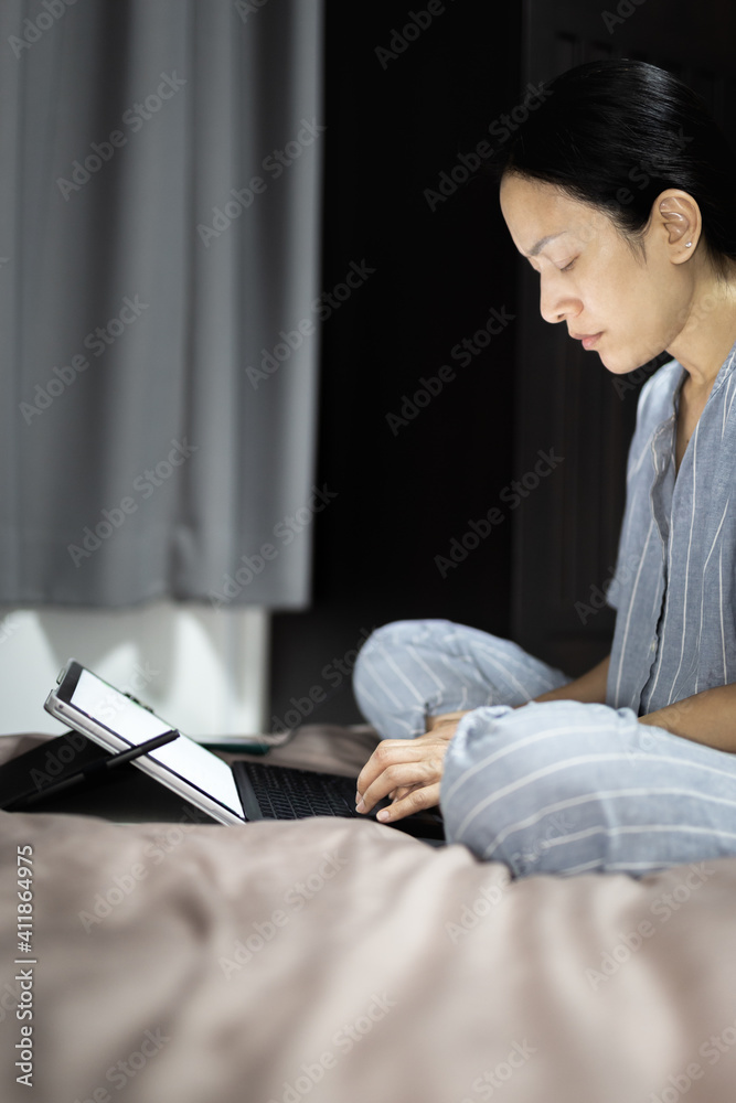 Naklejka premium Asian woman working with laptop computer in bed at night.