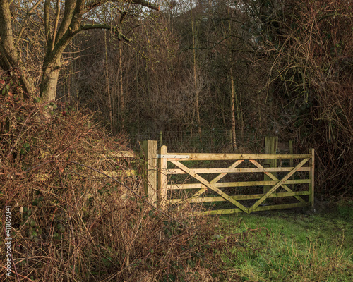An old-fashioned wooden five-barred gate at the entrance to a wood-lined field
