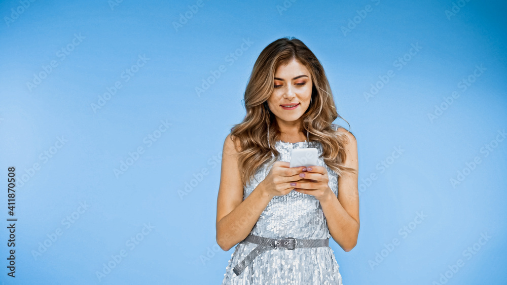 woman with wavy hair texting on smartphone while biting lips on blue woman with wavy hair texting on smartphone while biting lips on blue