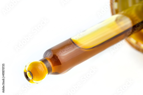 A macro shot of a glass pipette and a drop of CBD oil from cannabis extract, isolated on white.