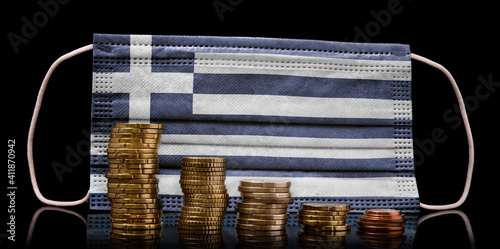 Medical mask with the flag of Greece behind some shrinking stacks of various coins.(series) photo