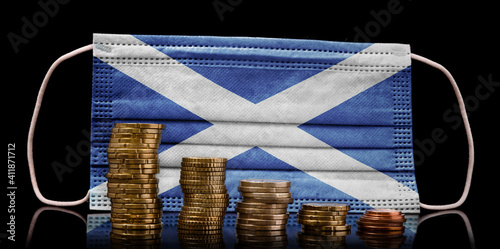 Medical mask with the flag of Scotland behind some shrinking stacks of various coins.(series) photo