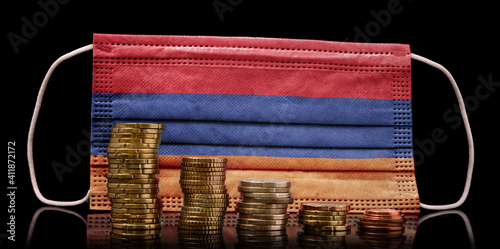 Medical mask with the flag of Armenia behind some shrinking stacks of various coins.(series) photo