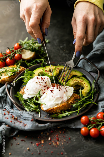 chef preparing foodbreakfast with poached egg on a slice of fried bread, avocado, arugula, cherry tomatoes and spices. Served in a cast-iron skillet, served with textiles on a black background