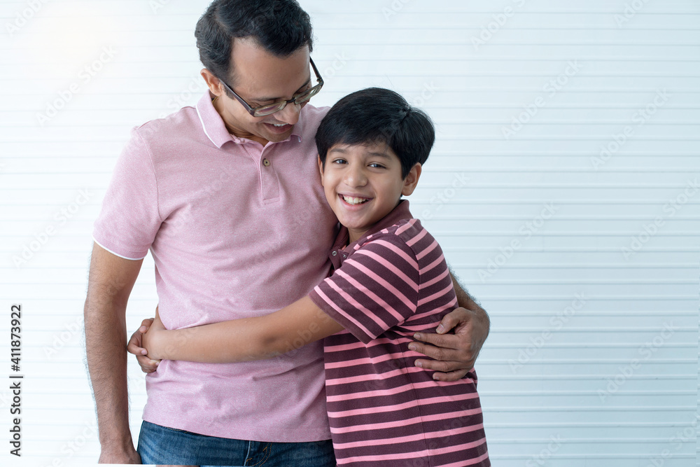 Happy Indian dad and son hugging and smiling at camera on white wall Happy Indian dad and son hugging and smiling at camera on white wall