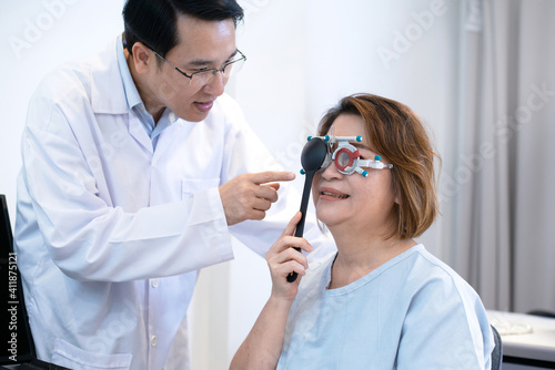 Senior Asian female patient holding  occluder to covering one eye to check her vision  optometrist advises her nearby