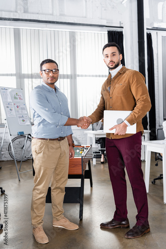 Multiethnic businessmen with laptop handshaking in office