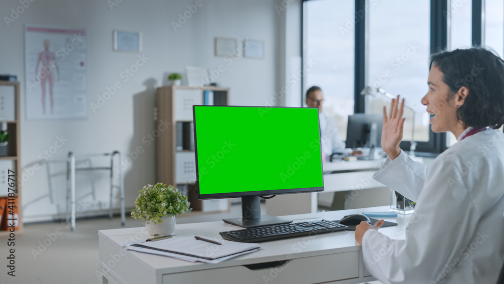Female Medical Doctor is Making a Video Call with Patient on a Computer with Green Screen Mock Up Display in a Health Clinic. Assistant in Lab Coat is Talking About Health Issues in Hospital Office. 