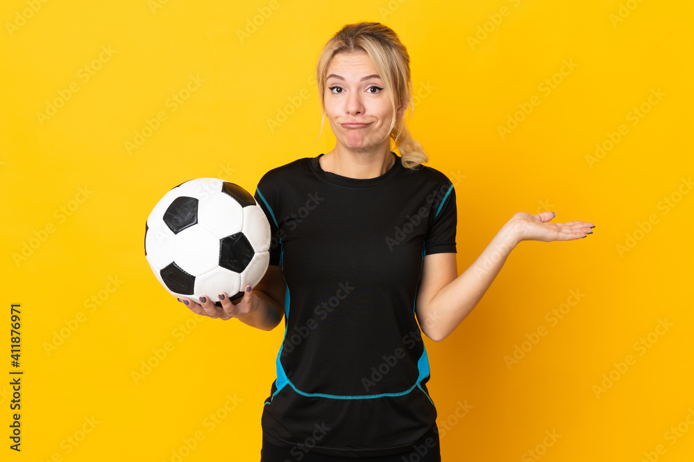 Young Russian football player woman isolated on yellow background having doubts while raising hands Young Russian football player woman isolated on yellow background having doubts while raising hands