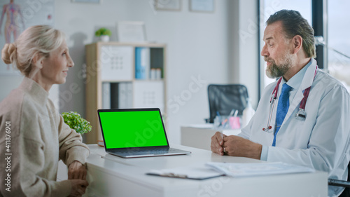Family Medical Doctor is Explaining Diagnosis to a Senior Patient on a Computer with Green Screen in a Health Clinic. Assistant in White Lab Coat is Reading Medical History in Hospital Office. 