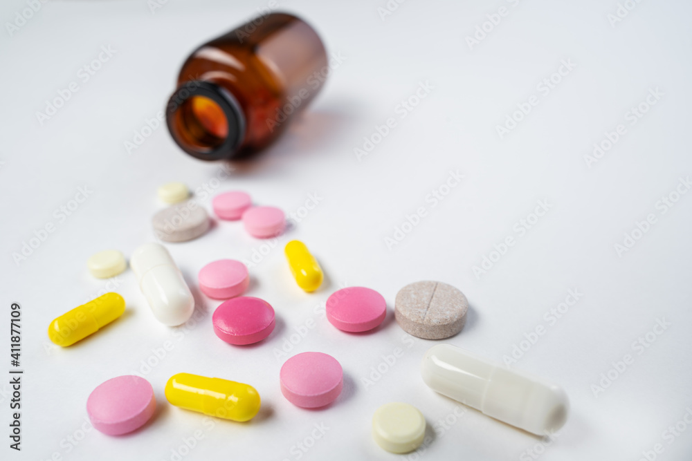 Multicolor pills and tablets spilling out from glass pill bottle on white. Multicolor pills and tablets spilling out from glass pill bottle on white.