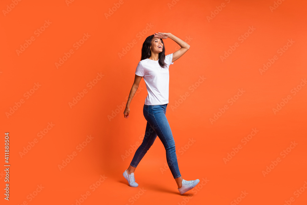 Full length photo of girl walk look empty space palm forehead wear white t-shirt jeans sneakers isolated orange color background Full length photo of girl walk look empty space palm forehead wear white t-shirt jeans sneakers isolated orange color background
