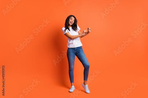 Full length photo of girl dance have fun wear white t-shirt jeans footwear isolated orange color background
