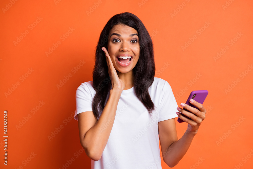 Photo of impressed girl hold telephone hand cheek wear white t-shirt isolated on orange color background - obrazy, fototapety, plakaty 