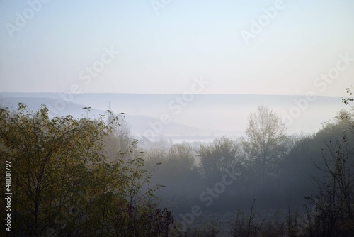 sunrise with fog in the forest colored in green and yellow. early autumn landscape in the wild