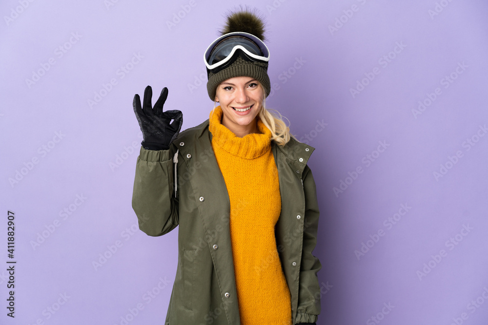 Skier Russian girl with snowboarding glasses isolated on purple background showing ok sign with fingers Skier Russian girl with snowboarding glasses isolated on purple background showing ok sign with fingers