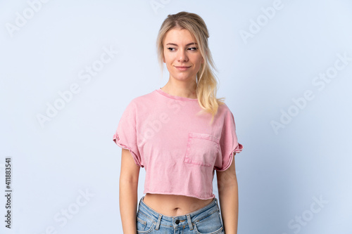 Blonde woman over isolated blue background having doubts while looking side