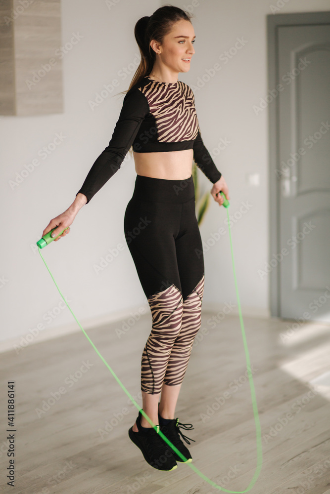 Athletic woman in sportswear does exercises and jump rope. Attractive woman in studio