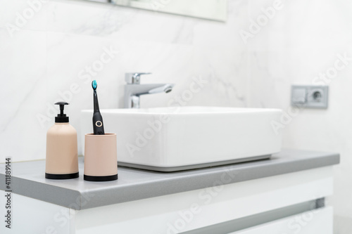 Photography Electric toothbrush in cup and soap dispenser bottle near basin
