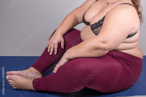 Yoga-Pose einer Rubensfrau mit langen br  netten Haaren    ppigem Busen  breiten H  ften und dickem Bauch  bekleidet mit schwarzem Oberteil und dunkelroter Leggins  auf einer blauen Gymnastikmatte
