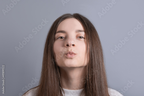 Young beautiful woman portrait with dark hair wearing white sweater show kiss show ideal lips send air kisses .Studio shot on gray background .Copy space.