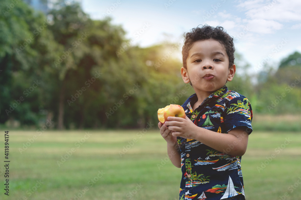 Portrait of half African half Asian 4 year old child happy to eat an apples at outdoor park, healthy fruit for children