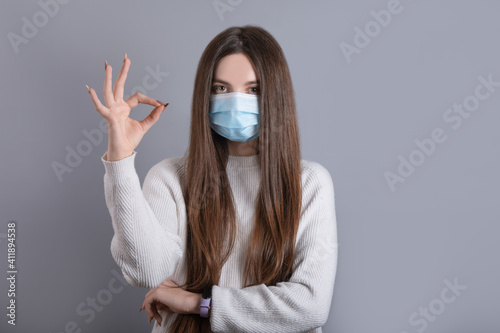 European girl in a medical mask, shows ok. Conceptual photo on the theme of the Covid 2019 pandemic. Studio photo.girl enjoy corona virus safety protection respiratory mask approve quality show okay  © Ivan