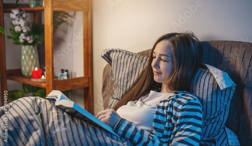A young woman is reading a book in bed before going to bed in a dark bedroom. Concept of the bedtime, and bedtime rituals for relaxation and healthy sleep