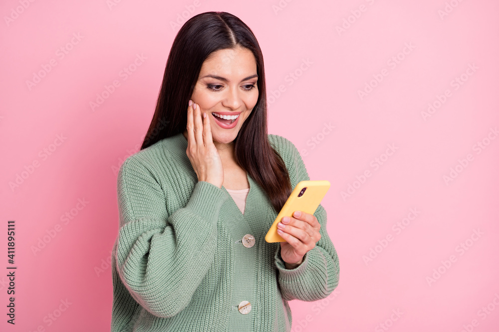 Photo of excited girl hold phone palm cheek open mouth wear green cardigan isolated pastel pink color background Photo of excited girl hold phone palm cheek open mouth wear green cardigan isolated pastel pink color background