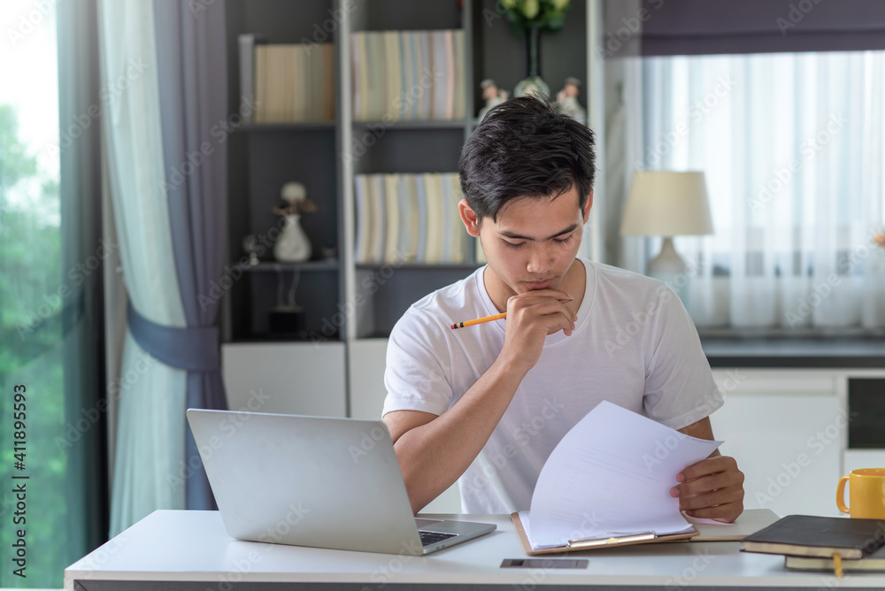 Image of young Asian businessman analyzing work using a laptop at home. Image of young Asian businessman analyzing work using a laptop at home.