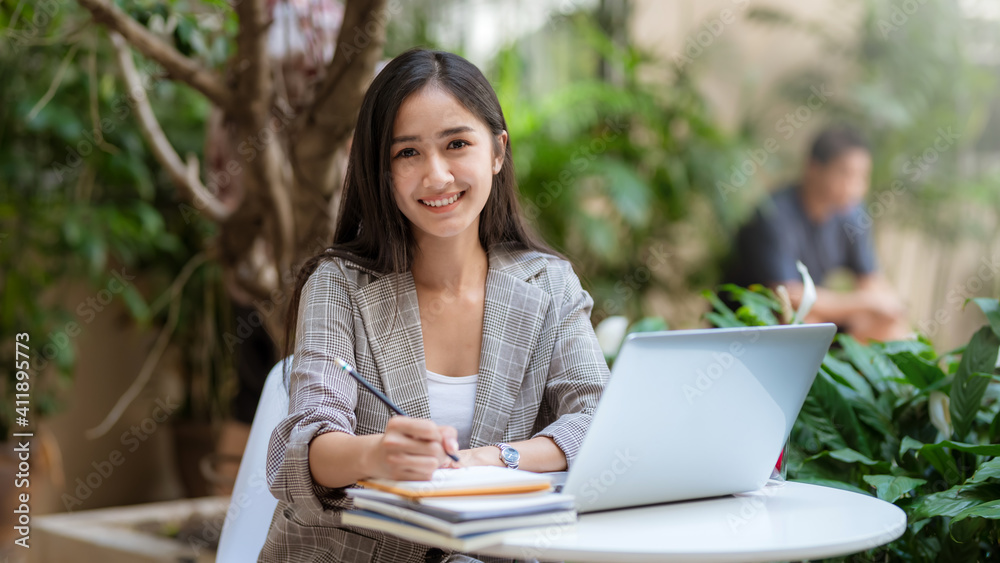 Asian businesswoman smiles at the camera while working in a casual laptop garden at a coffee shop. Asian businesswoman smiles at the camera while working in a casual laptop garden at a coffee shop.