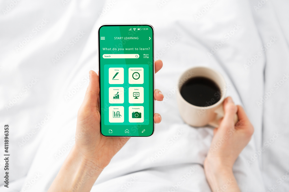 Woman using smartphone with educational app on screen while relaxing in bed Woman using smartphone with educational app on screen while relaxing in bed