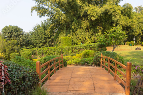A wooden bridge with handrails over a stream in a park with lush green surroundings