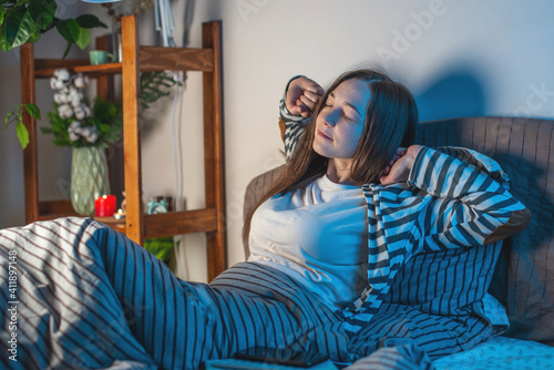 A young happy woman is lying in her cozy bed, stretching and getting ready for bed. Concept of bedtime pastime and rituals for a healthy and restful sleep