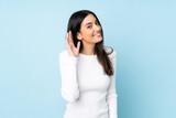 Young caucasian woman isolated on blue background listening to something by putting hand on the ear