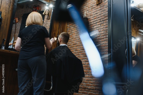 Stylish man sitting barber shop Hairstylist Hairdresser Woman cutting his hair Portrait handsome happy young bearded caucasian guy getting trendy haircut Attractive barber girl working serving client © Serhii