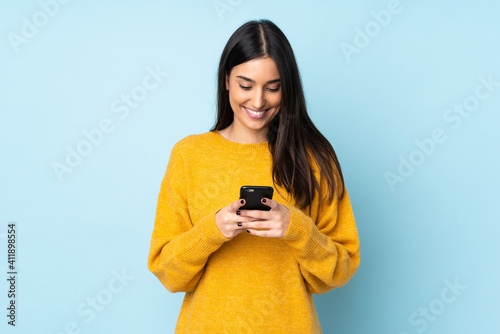 Young caucasian woman isolated on blue background sending a message with the mobile photo