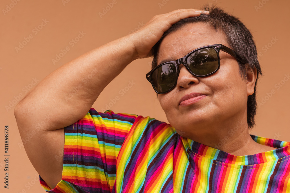 Androgynous close up portrait of asian Middle-aged women posing in cool rainbow shirt on orange background. Androgynous close up portrait of asian Middle-aged women posing in cool rainbow shirt on orange background.