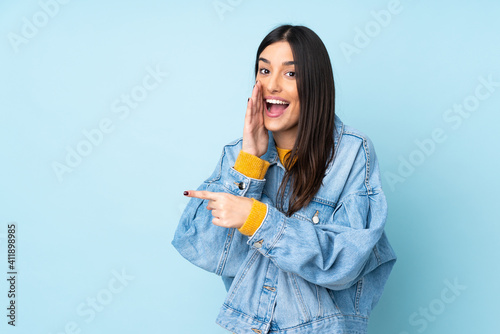 Young caucasian woman isolated on blue background pointing to the side to present a product and whispering something