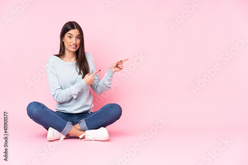 Young caucasian woman isolated on pink background frightened and pointing to the side