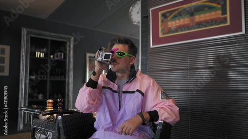 An unusual freaky guy from the 80s or 90s in purple clothes, in his hand he has an old video camera that works from a tape cassette.