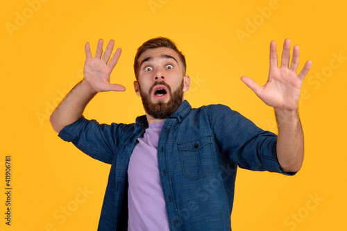 Scared Caucasian man making frightened gesture with his hands, trying to defend himself on orange studio background photo