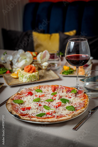 Vertical shot of pizza with vegan ingredients served with a glass of wine and salad in restaurant photo