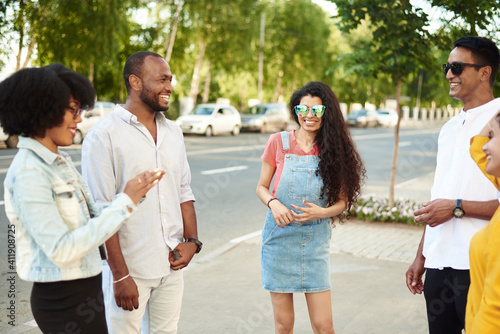 Young people having fun outdoors. A group of multi-ethnic friends are talking and laughing while standing in the street