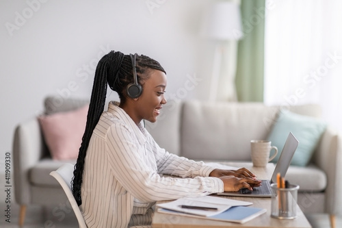 Positive black woman with headphones sitting in front of laptop