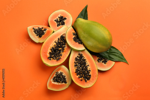 Fototapeta Naklejka Na Ścianę i Meble -  Fresh ripe papaya fruits with green leaves on orange background, flat lay