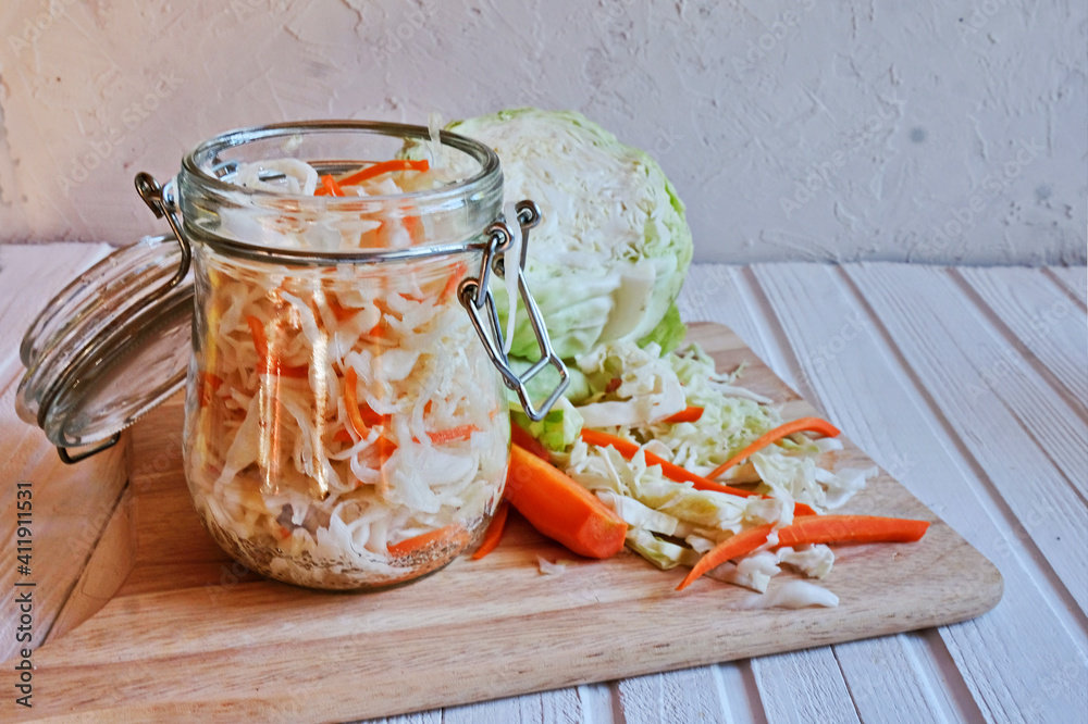 Homemade sauerkraut with carrots in a glass jar on wooden table. Fermented vegetables. Vegetarian vegan food. Sauercraut- cut, fermented cabbage, german and russian style cuisine.